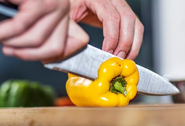 Un pimentón amarillo siendo cortado con un cuchillo.