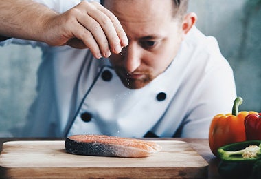 El pescado se debe sazonar antes de llevarlo a la freidora de aire. Chef sazonando un pescado antes de hacerlo en la freidora de aire.