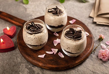 Los postres en vaso pueden ser chocolate, frutas y muchos otros ingredientes. Postre de chocolate y galletas en vaso, sobre una bandeja decorada con pétalos.