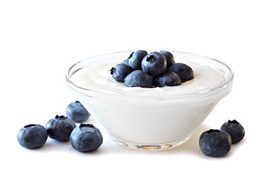 El yogurt griego es un alimento versátil que combina muy bien con frutas Recipiente de vidrio con yogurt griego y arándanos