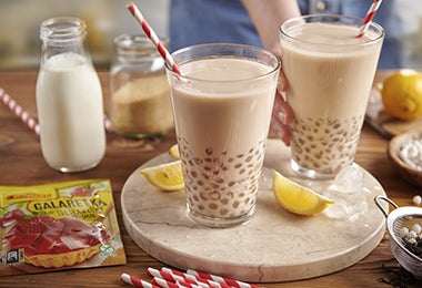 Dos vasos con bebida de perlas de tapioca, juntos a tarros de leche, limones y azúcar.