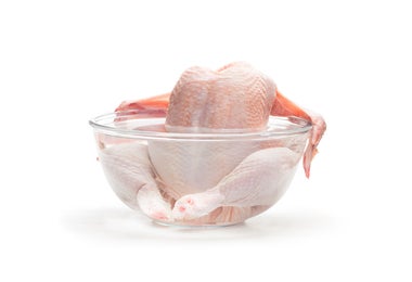 Carcasa de pollo cruda sumergida en un bowl de agua transparente, lista para cocinar un caldo de hueso de pollo casero
