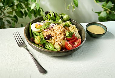 Ensalada Nicoise servida en un bowl oscuro, acompañada de un tenedor y vinagreta en un pequeño recipiente