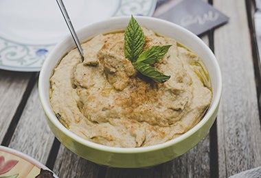 Hummus con unas hojas aromáticas y una cuchara en una mesa, un plato frío ideal de acompañamiento