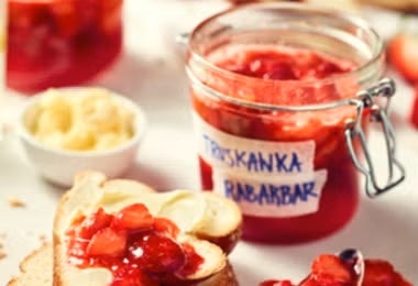 Mermelada de ruibarbo y frutillas servida sobre tostadas con frascos en el fondo