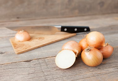 Cebolla cortada a la mitad en tabla de picar para ser cortada en julianas con el método tradicional.