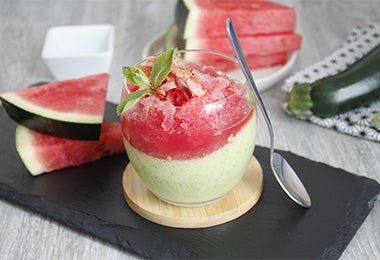 Vaso de panna cotta de frutas tropicales junto a pedazos de sandía.