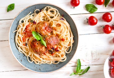 Plato de pasta a la boloñesa con tomates al lado para comer con pan bolillo.