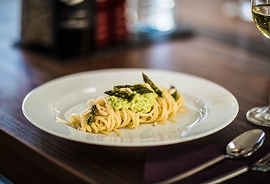 Pasta pesto servida con hierbas en una mesa con sal, pimienta y cubiertos