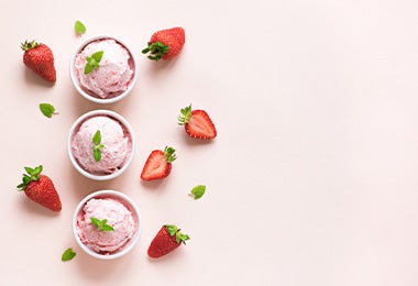 Tres vasos de helado decorados con hojas y rodeados de fresas frescas es un postre sin gluten ideal