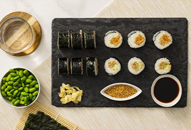 Doce rollos de sushi con salsa de soya y semillas de sésamo sobre un plato negro