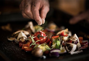 Mano espolvoreando sal como alimento de origen mineral sal sobre vegetales frescos como tomate, champiñón y cebolla