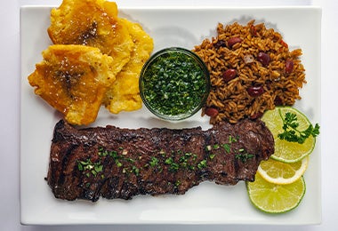  Un plato con chimichurri, carne, arroz y patacones