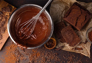 Chocolate derretido en un bowl y un ponqué de chocolate para preparar una Tarta Sacher.