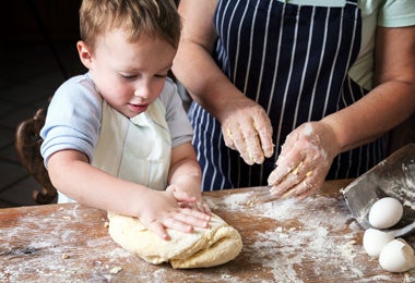 Pequeño niño ayudando a persona adulta a amasar masa para pan bolillo.