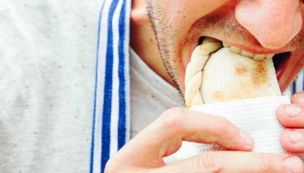 Un hombre comiendo una empanada tucumeña, una clase de empanada argentina.