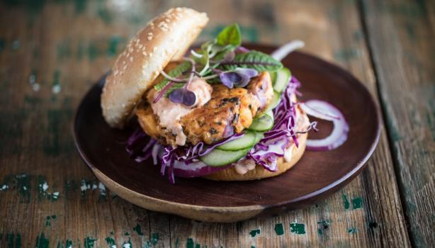 Apetitosa hamburguesa de pescado con vegetales emplatada y sobre una mesa de madera-