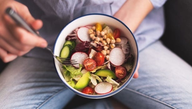 Bowl de comida vegana sostenida por una persona mientas come.