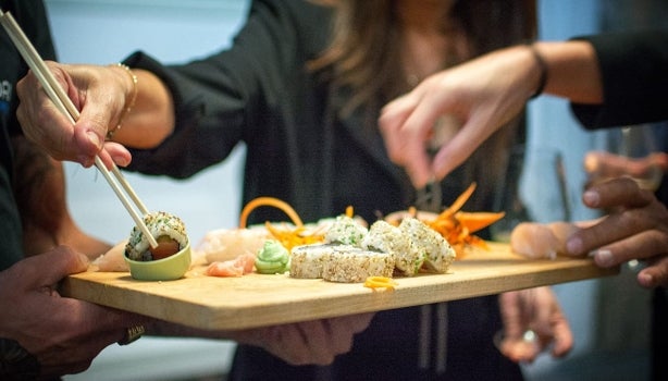 Varias personas degustando una tabla de sushi vegano.