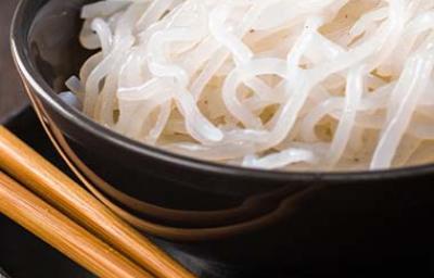 Los noodles de arroz se usan para acompañar diferentes platos Noodles de arroz, servidos en un plato negro, junto a unos palillos chinos.