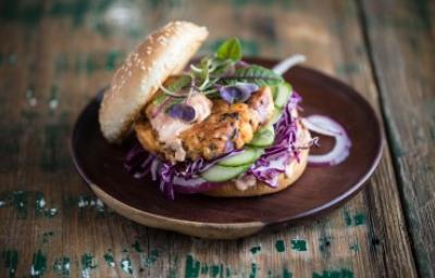 Apetitosa hamburguesa de pescado con vegetales emplatada y sobre una mesa de madera-