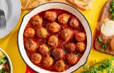 Albóndigas caseras en salsa putanesca servidas en una sartén con cebollas y cilantro