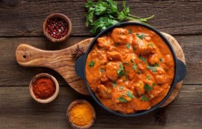 Butter Chicken con cilantro y acompañado de especias sobre tabla de madera