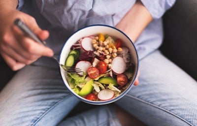 Bowl de comida vegana sostenida por una persona mientas come.