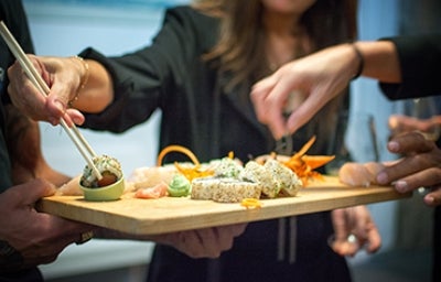 Varias personas degustando una tabla de sushi vegano.
