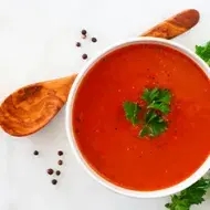 Crema de tomate con perejil, una de las recetas más famosas, servida con una cuchara de madera.