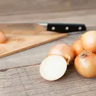 Tabla de corte y cuchillo con cebollas enteras y en mitades  