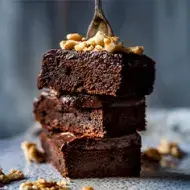Plato con tres pisos de brownie espolvoreado con nueces, este es un postre sin gluten 