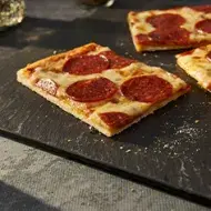 Porción de pizza de pepperoni con una masa delgada sobre un plato negro para celebrar su Día Mundial