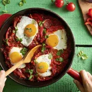  Huevos shakshuka con hierbas, salsa de tomate, pan y pimentón picado en toma cenital.