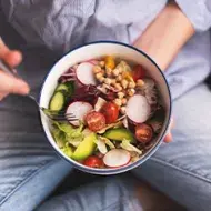 Bowl de comida vegana sostenida por una persona mientas come.