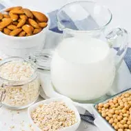 Jarra de vidrio de crema vegetal de almendras, junto a snacks de frutos secos.