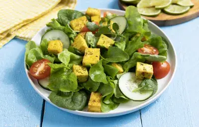Ensalada fresca con cubos de tofu marinado dorado, pepino, tomate y hojas verdes