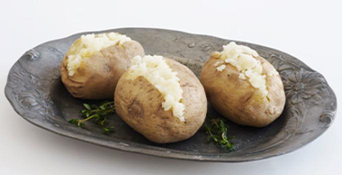 Las papas son comidas fáciles de hacer que pueden completar una cena. Tres papas sobre un plato negro, una comida fácil de hacer en casa.