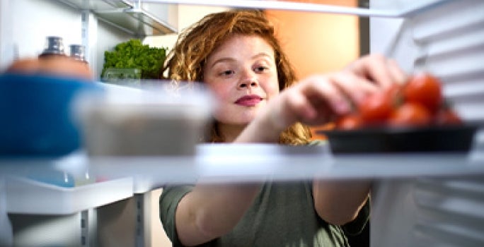 Mujer refrigerando tomates, quitar mal olor del refrigerador Mujer refrigerando tomates, quitar mal olor del refrigerador