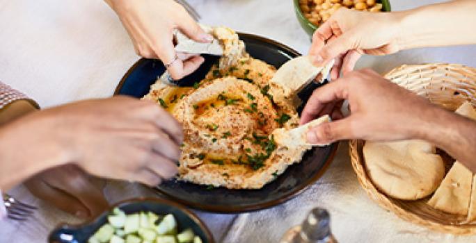 El hummus es tradicional en la comida libanesa. Un grupo de personas compartiendo hummus con pan pita, un clásico de la comida libanesa